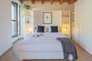 Une chambre bien rangée, avec un grand lit, des tables de chevet, un tableau encadré au mur et une fenêtre agrémentée d’une plante.