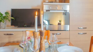 A dining area with a table set for two, a lit candle, and a television in the background.