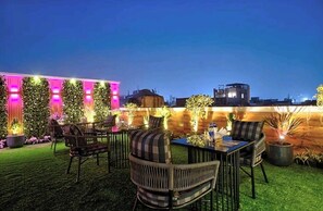 An outdoor seating area with tables and chairs, surrounded by potted plants and illuminated by pink lights. - Hotel Hanuwant Palace  (New Delhi)