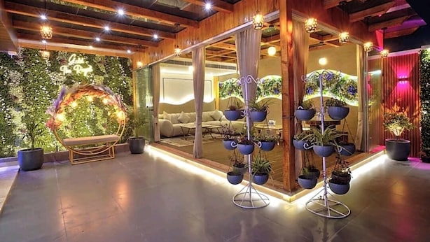 Een modern interieur met een houten plafond, een zithoek met een bank en een lange bank, en een wand versierd met planten en een neonbord.