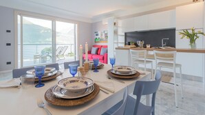 Ein moderner Essbereich mit einem großen Tisch, gedeckt für vier Personen, einer Küche und einem Balkon mit Bergblick.