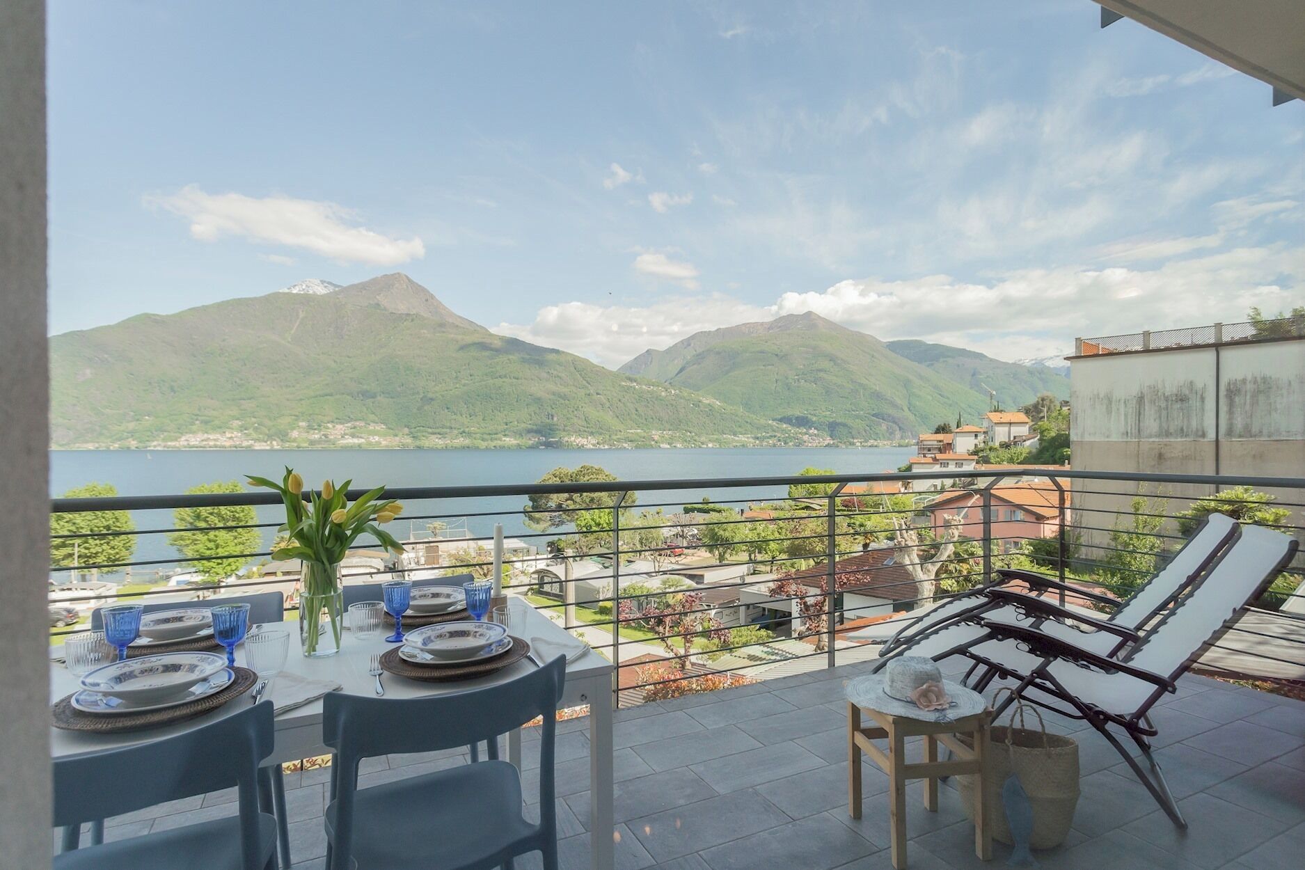A balcony with a table set for dining, overlooking a lake and mountains.