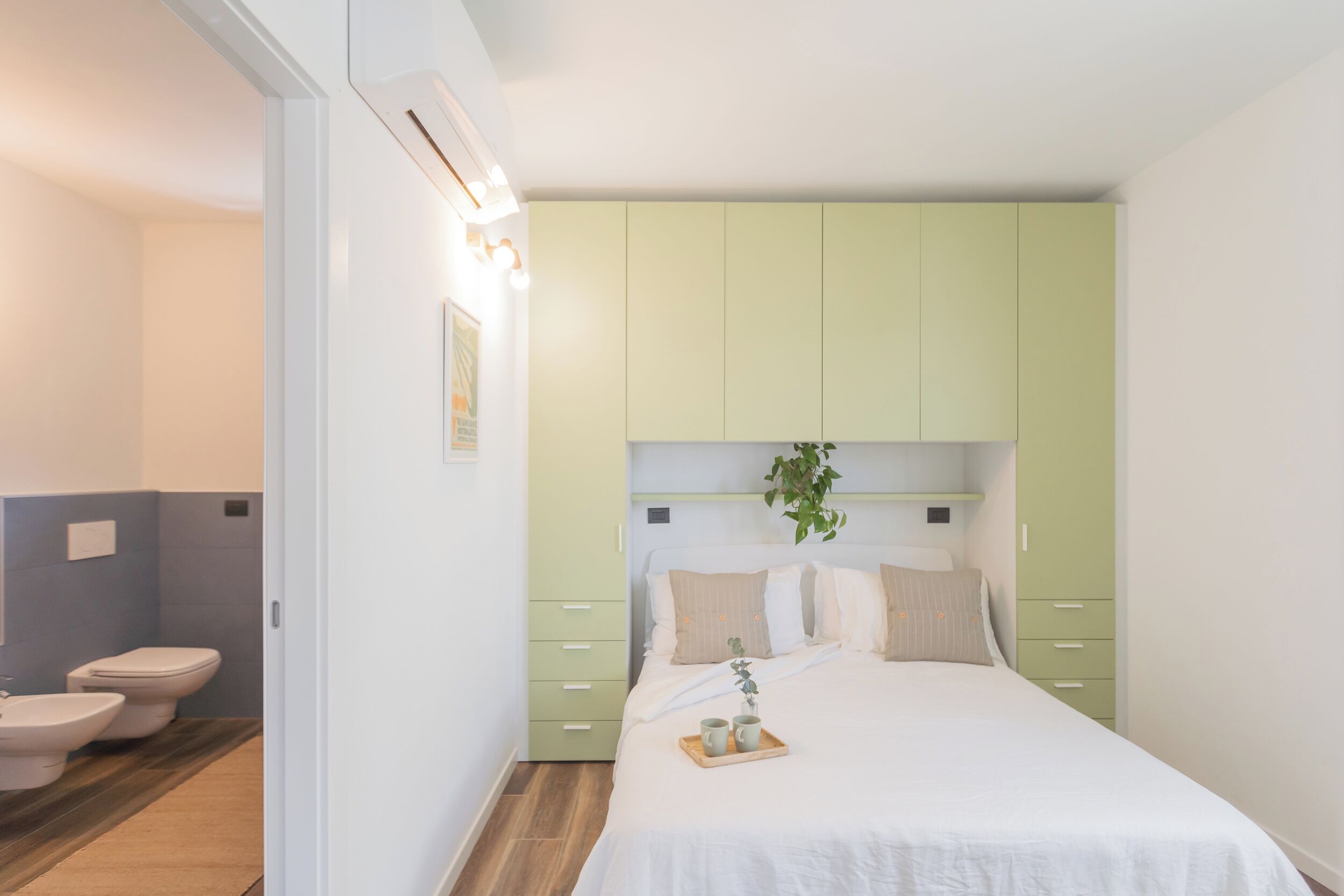 A bedroom with a bed, bedside tables, a green wardrobe, and a bathroom with a toilet and bidet.