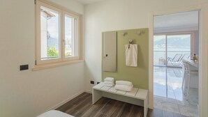 Ein Badezimmer mit Fenster, einem Spiegel, einer Sitzbank mit Handtüchern und Blick auf einen Balkon mit Stühlen und einem Tisch.