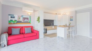 Eine moderne Wohnung mit einem roten Sofa, einer Küche mit weißen Schränken und einem Essbereich mit weißen Stühlen.