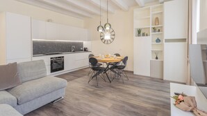 Una cocina moderna con armarios blancos, una mesa de comedor de madera y sillas negras. Cuenta con un horno empotrado y un reloj en la pared.