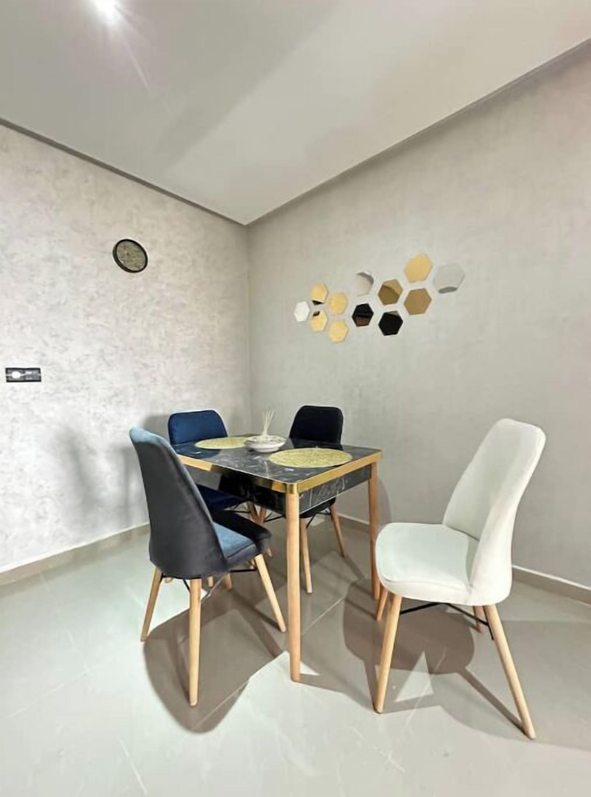 Un coin repas comprenant une table et quatre chaises, un luminaire fixé au mur et un motif hexagonal décoratif sur le mur.