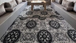 Ein gemütliches Wohnzimmer mit einer Sofagarnitur, einem Couchtisch, einem gemusterten Teppich und einer Deckenleuchte.