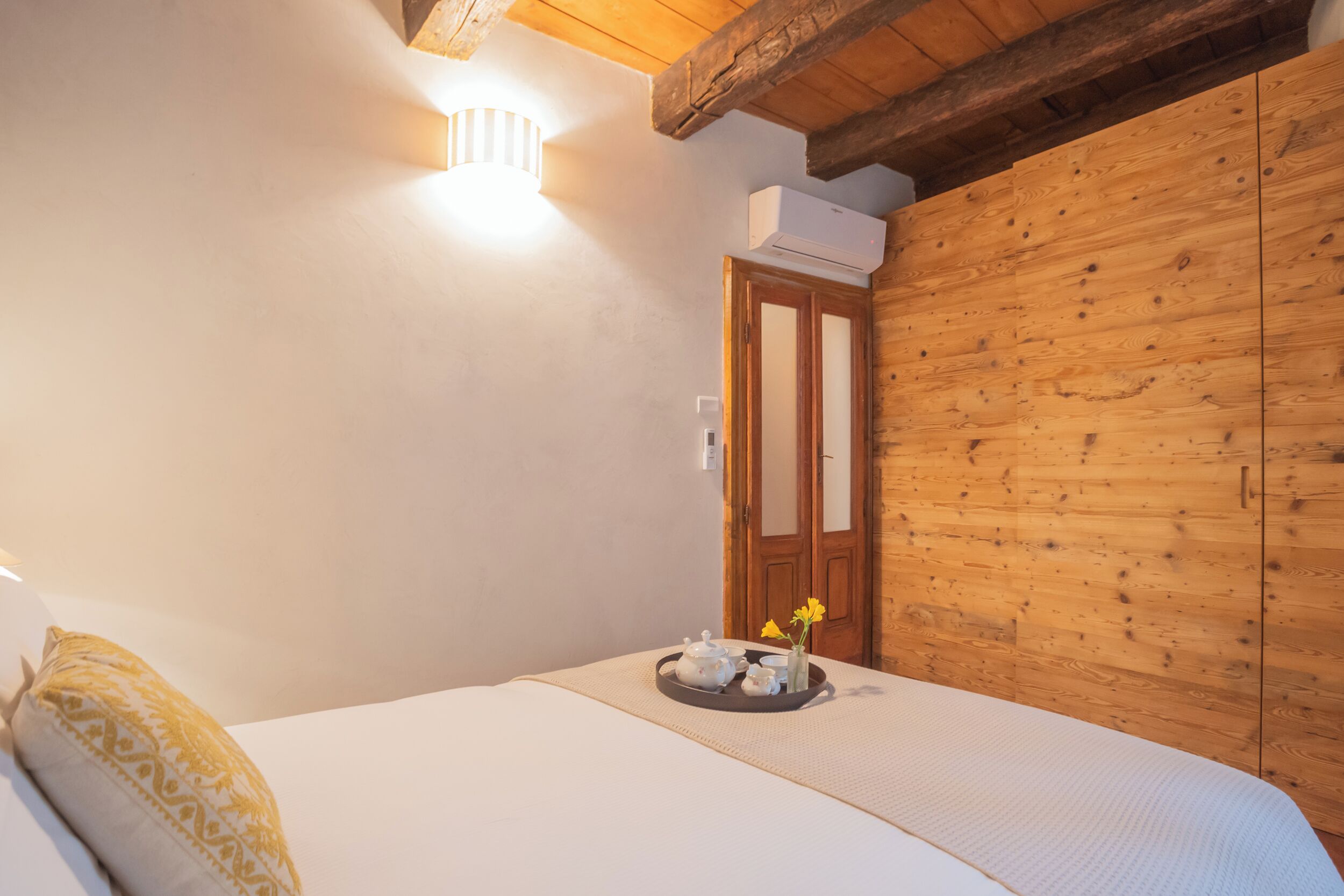Ein Schlafzimmer mit Holzboden, einem Bett mit weißer Bettdecke, einem Tablett mit Teezubehör und einer Wand-Klimaanlage.