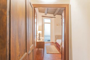 A narrow hallway with wooden doors leading to a bedroom with a bed, a radiator, and a window. - Pantero Apartment by Rent all Como (Como)