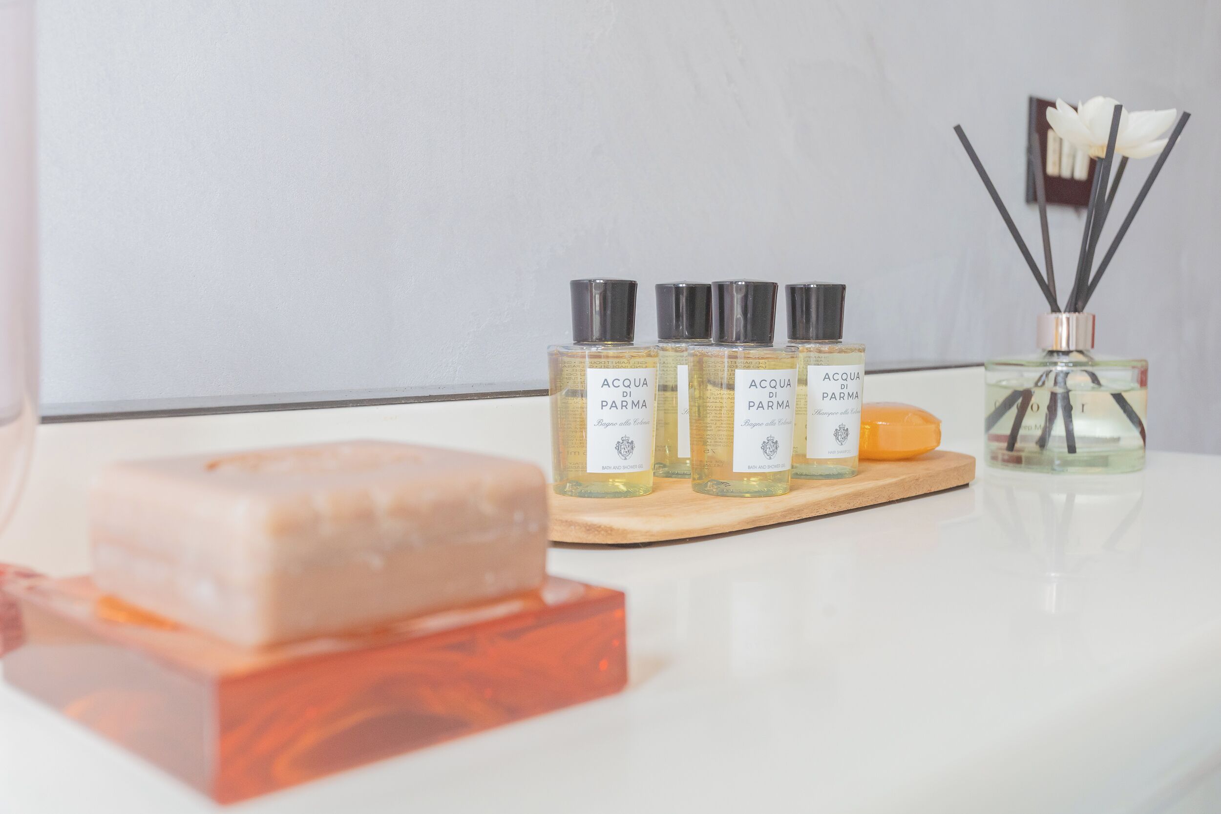 Tre flaconi di colonia Acqua di Parma, una saponetta e un diffusore di fragranze in rattan su una superficie bianca.