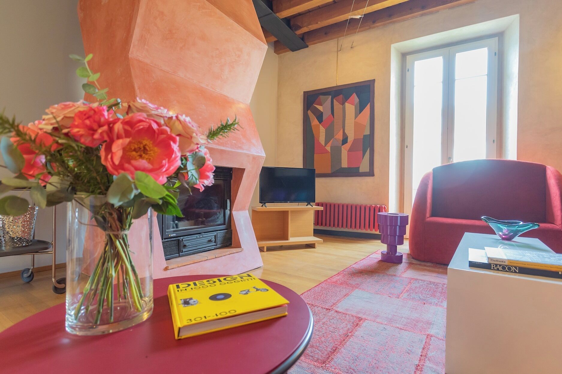 A living room with a fireplace, a red armchair, a television, and a vase of flowers.