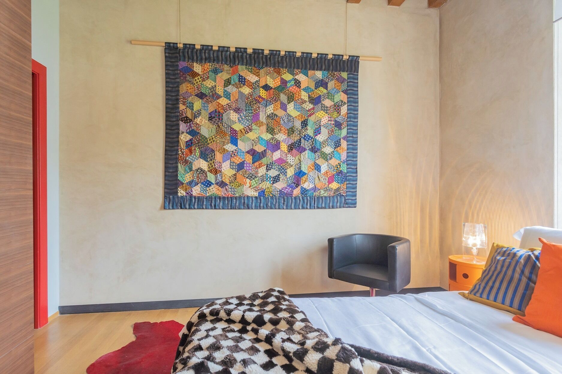 Ein Schlafzimmer mit einem großen Bett, einem Sessel, einem Nachttisch und einem farbenfrohen Wandteppich.