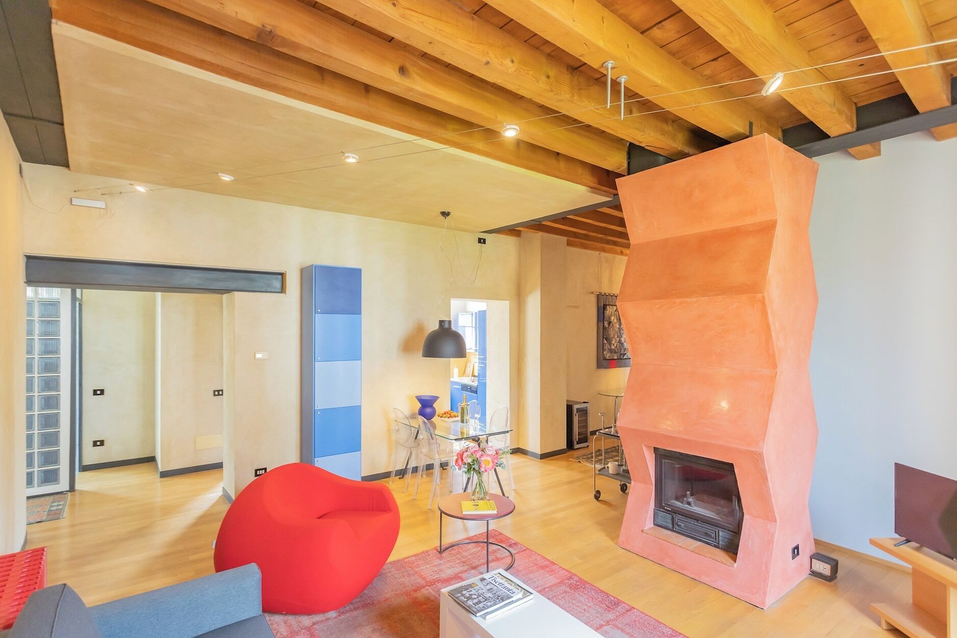 A modern living room with a wooden ceiling, a red bean bag chair, a fireplace, and a television.