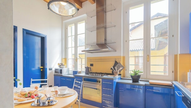 A modern kitchen with blue cabinets, a gas stove, a microwave, and a large window. - Night at the Museum Apartment by Rent all Como (Como)