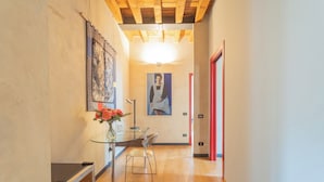 A hallway with wooden flooring, a glass table with a vase of flowers, a painting on the wall, and a red door at the end. - Night at the Museum Apartment by Rent all Como (Como)