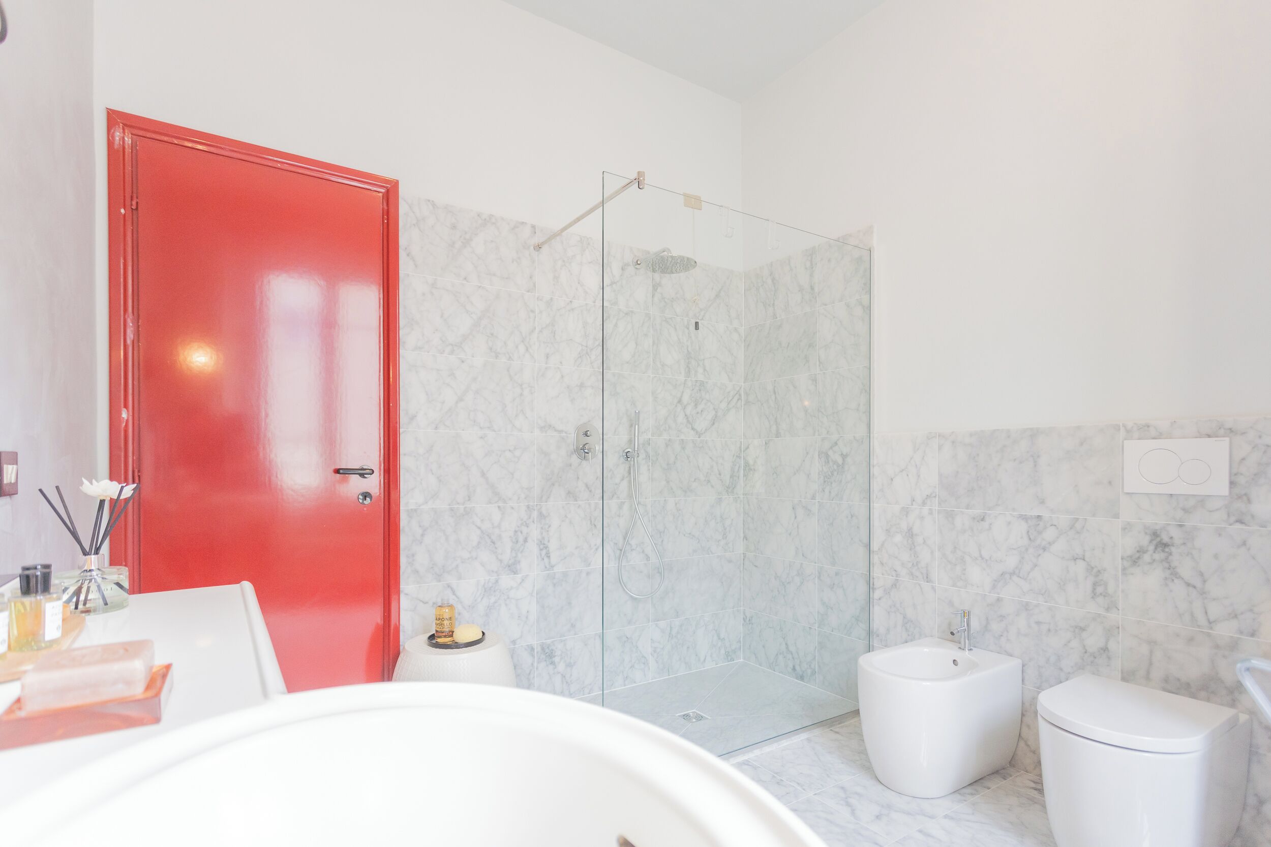 A modern bathroom with a glass-enclosed shower, a red door, and a white sink and toilet.