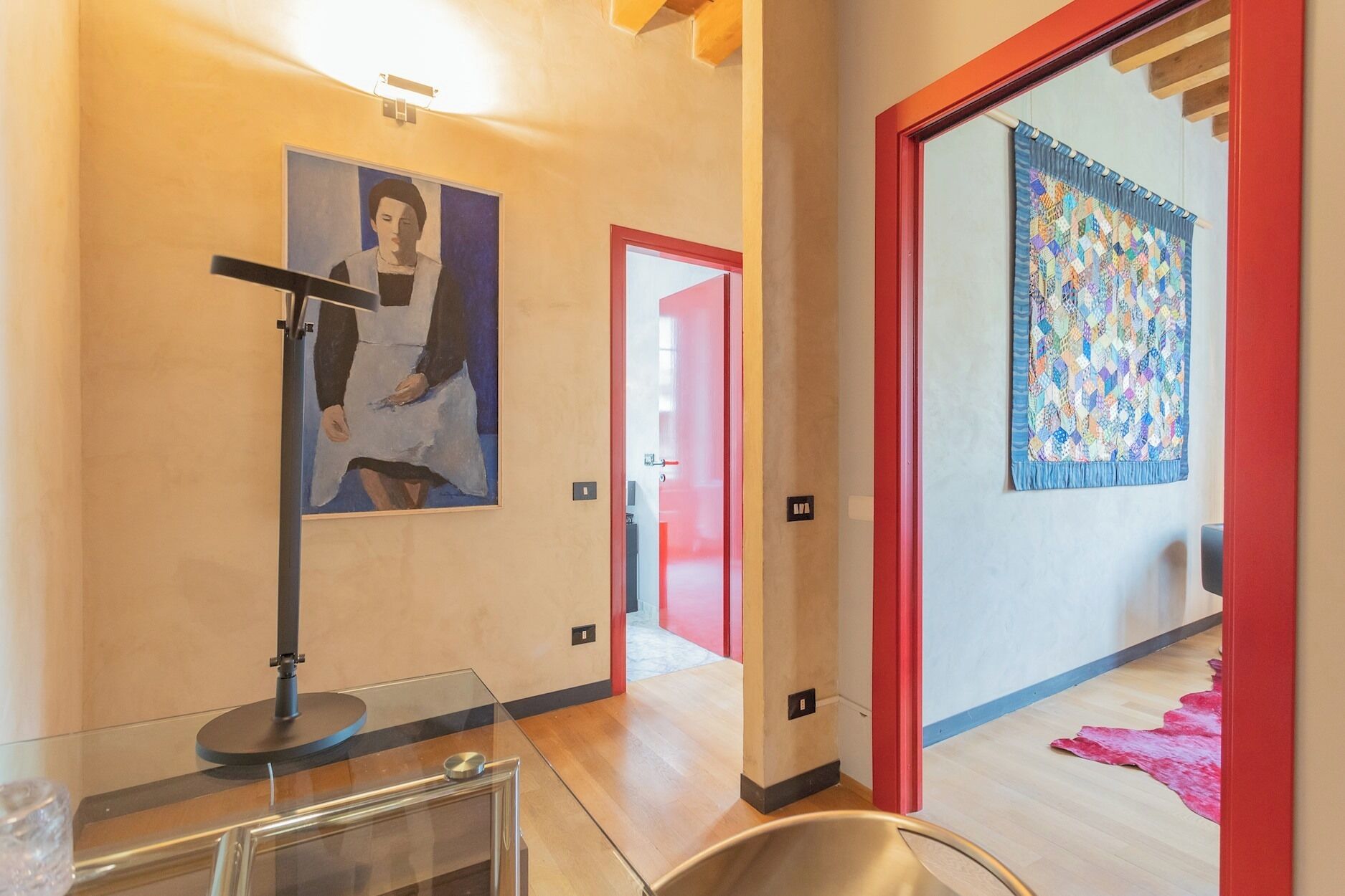 Un interior moderno con una vitrina de vidrio, un cuadro en la pared y un colcha colorida colgada en la puerta.