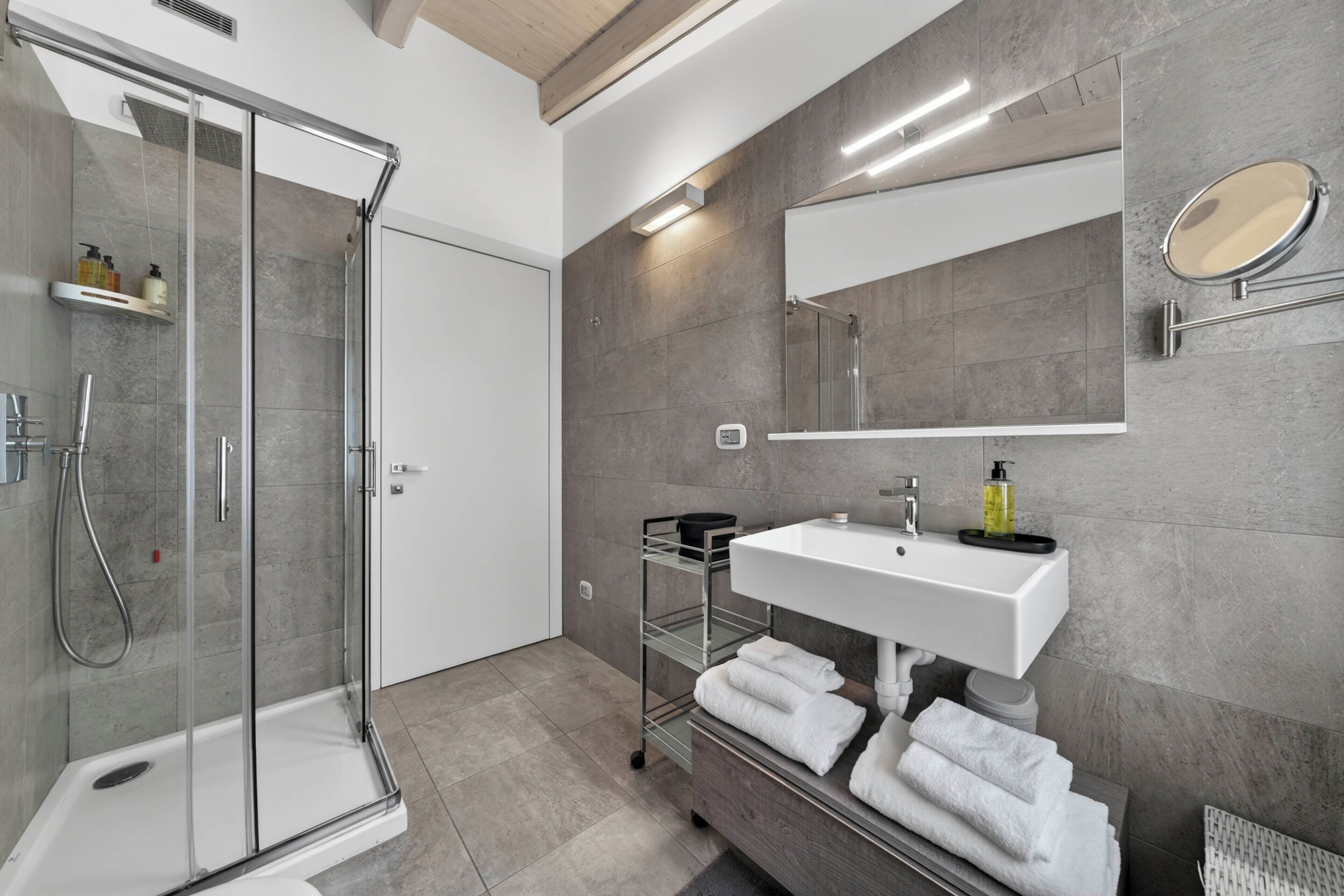 A modern bathroom with a glass shower enclosure, a white sink, and a mirror.