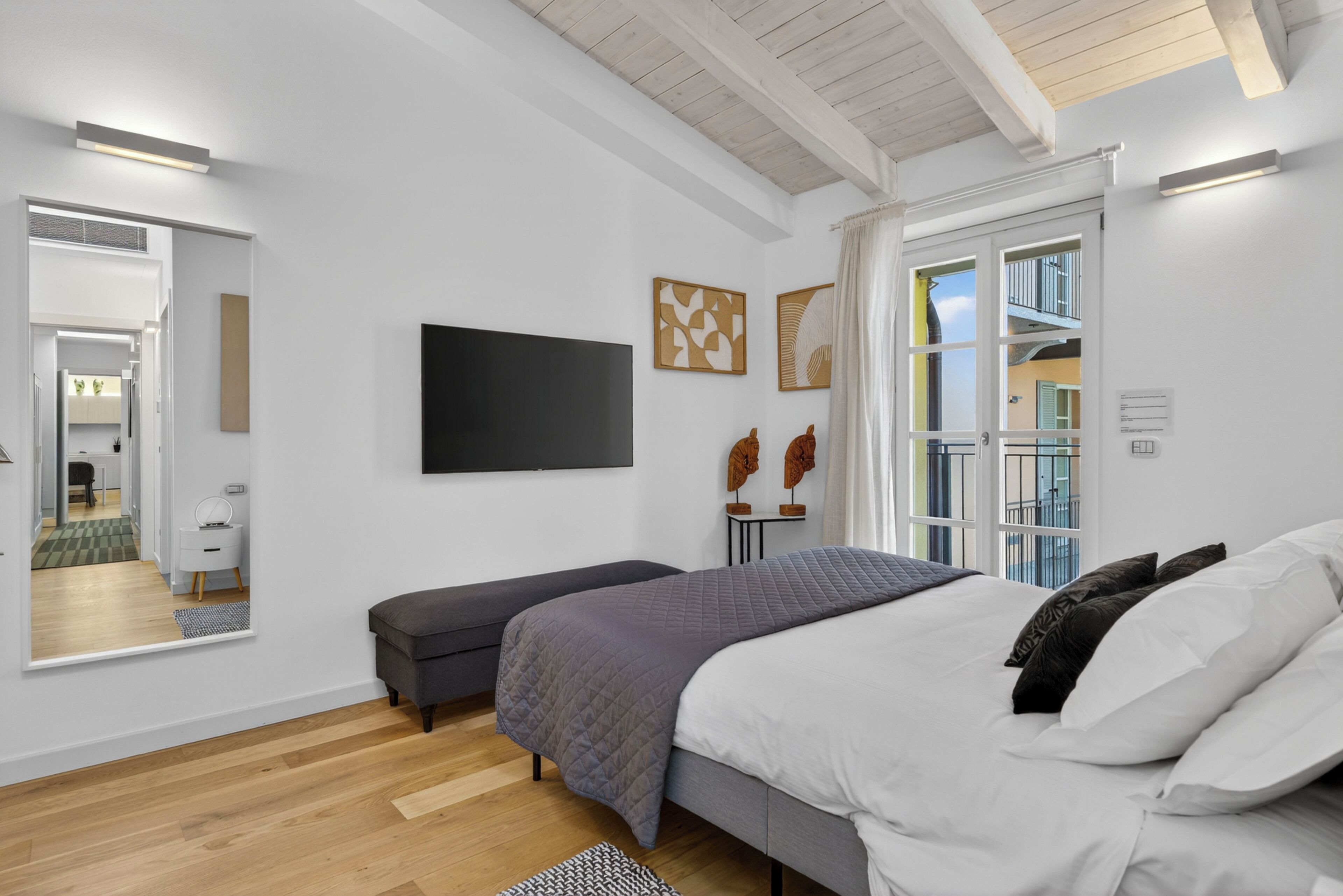 A modern bedroom with a bed, a bench, a TV, and artwork on the wall.