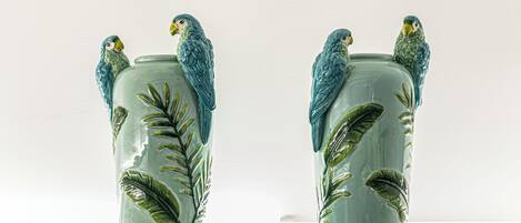 Two ceramic vases with parrot figurines and leaf patterns, placed on a shelf.