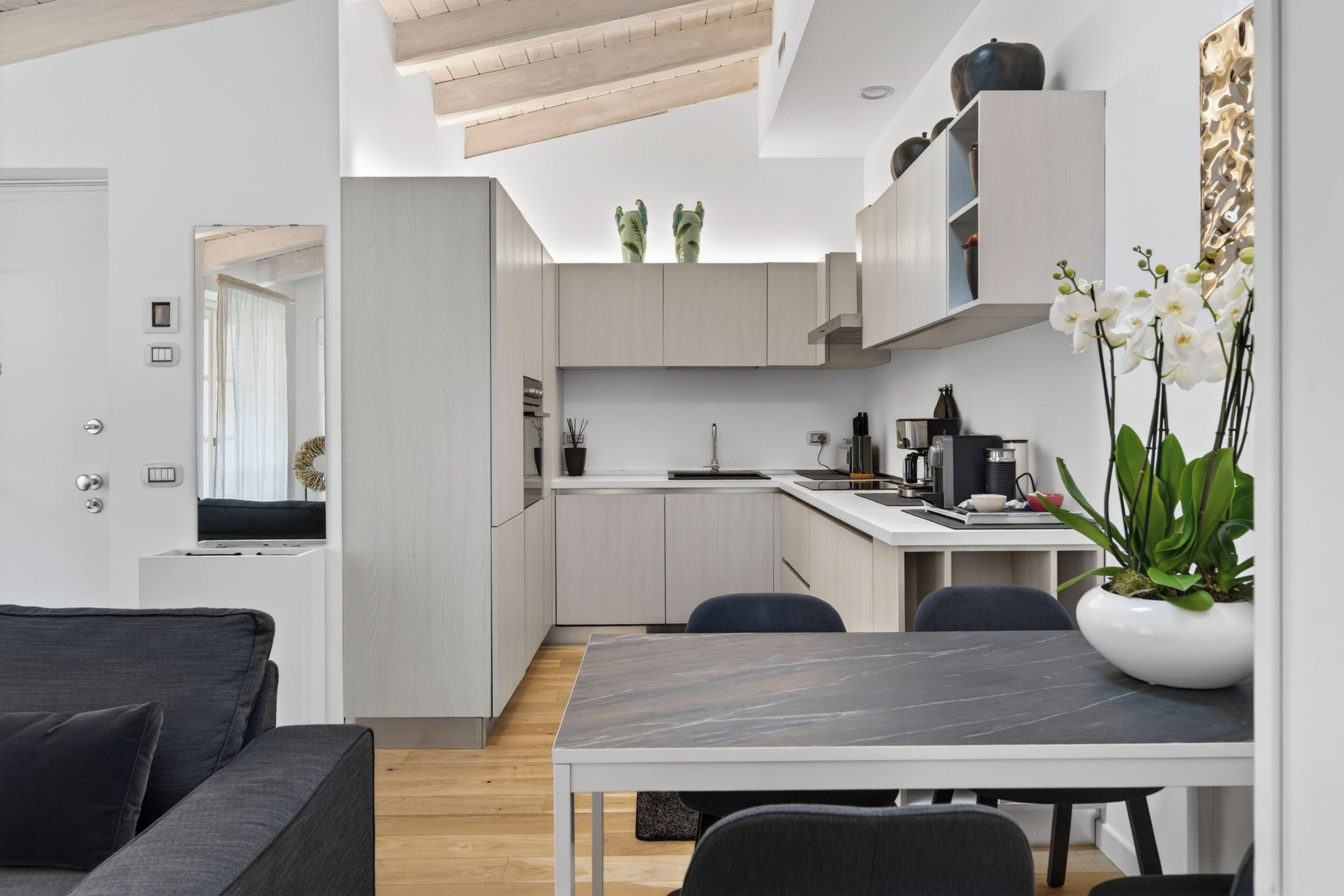 A modern kitchen with white cabinets, a dining table, and chairs. There is a plant on the counter and a vase with flowers on the table.