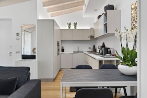 A modern kitchen with white cabinets, a dining table, and chairs. There is a plant on the counter and a vase with flowers on the table.