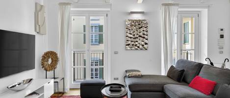 Un salon moderne avec un téléviseur à écran plat, un canapé gris, une petite table ronde et un tapis à motifs.