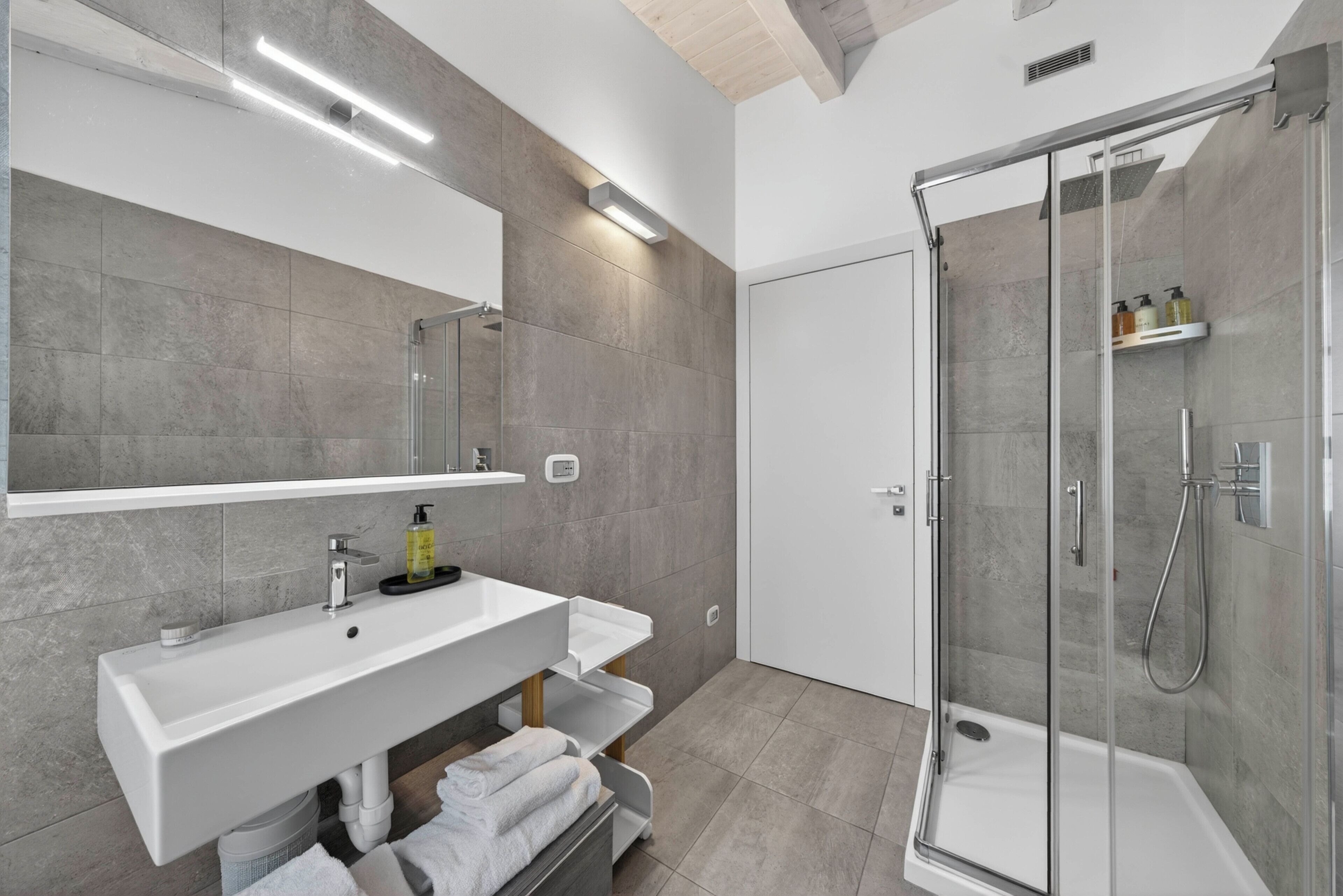 A modern bathroom with a glass shower enclosure, a white sink with a mirror above, and a towel rack.
