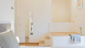 Une chambre à coucher moderne avec un lit, une table de chevet, un miroir et un petit banc en bois.