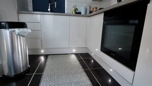A modern kitchen with white cabinets, a black tiled floor, a stainless steel trash bin, and a black oven. - Modern, Spacious 3 Bedroom home Watford Junction (Watford)
