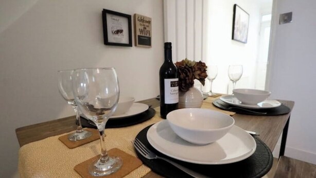 A dining table set with wine glasses, a bottle of wine, and bowls on a textured placemat. - Modern, Spacious 3 Bedroom home Watford Junction (Watford)