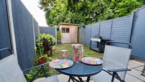 A patio with a round table and four chairs, surrounded by a wooden fence and a shed. - Modern, Spacious 3 Bedroom home Watford Junction (Watford)