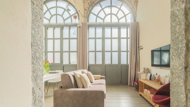 A spacious living room with a large window, a sofa, a wooden TV stand, and a dining area. - Romantic Escape City Centre With Jacuzzi & Parking by Rent all Como (Como)