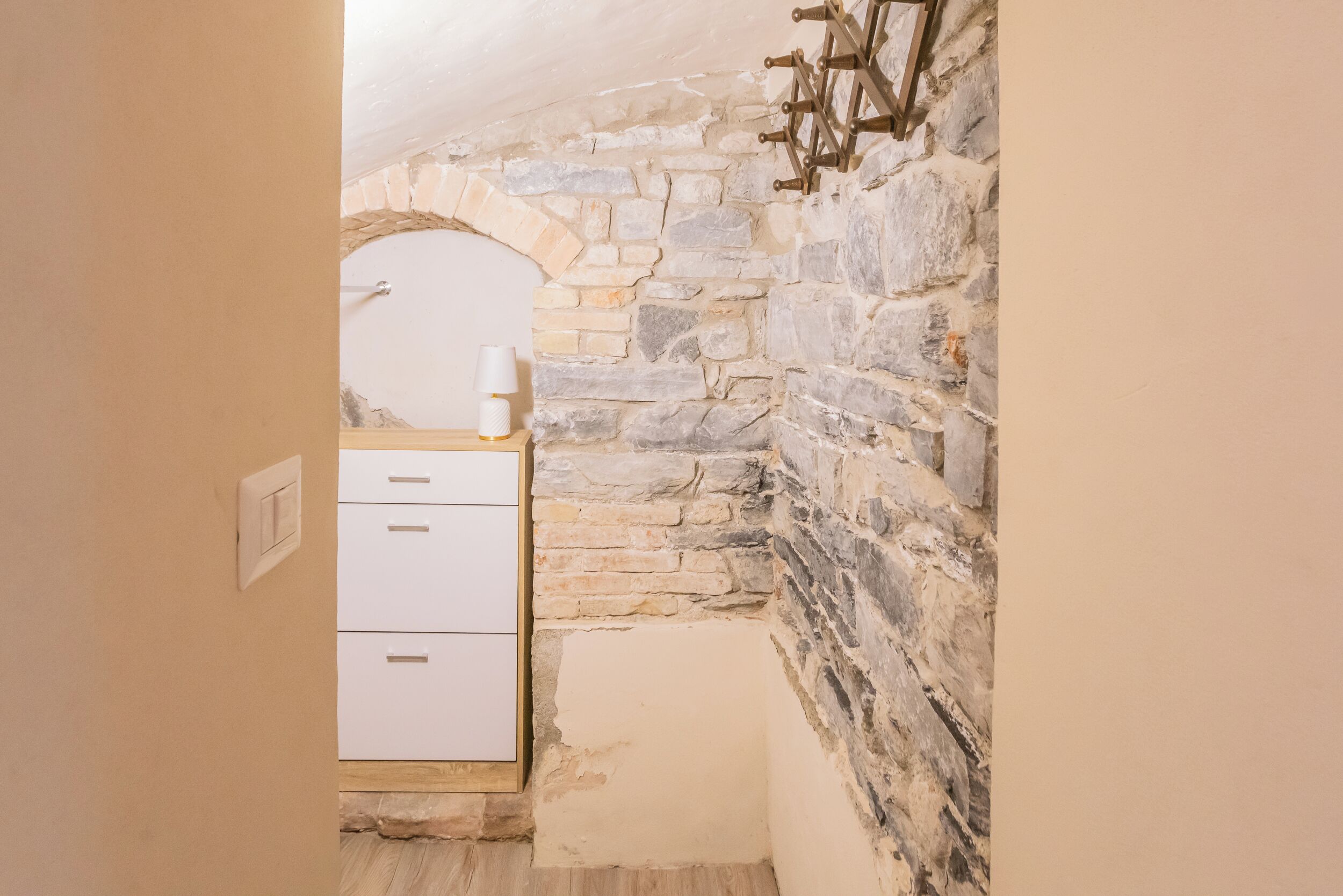 A narrow room with a stone wall, a white cabinet, and a small table with a lamp.
