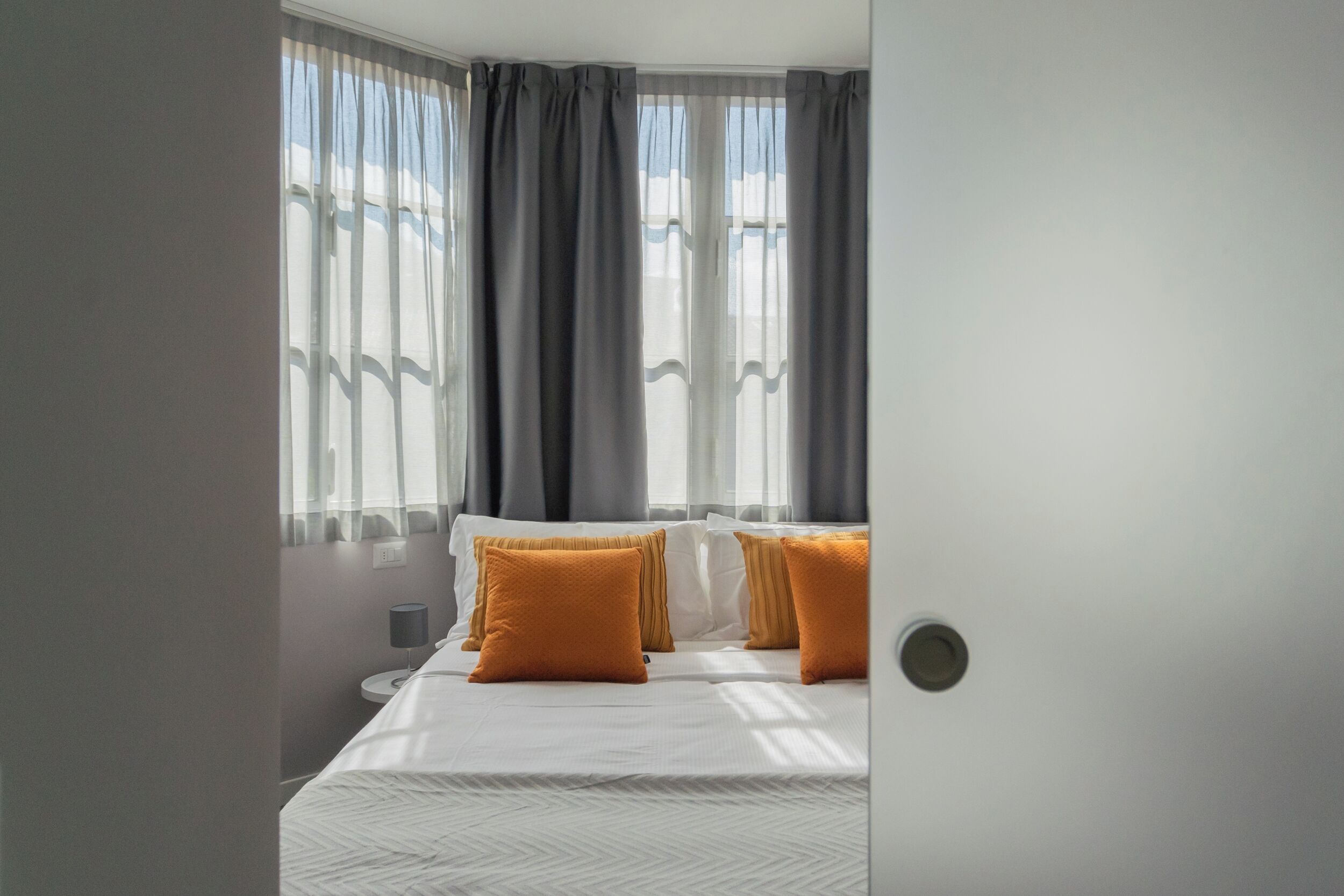Una habitación de hotel con una cama, una mesita de noche y un ventanal con cortinas.