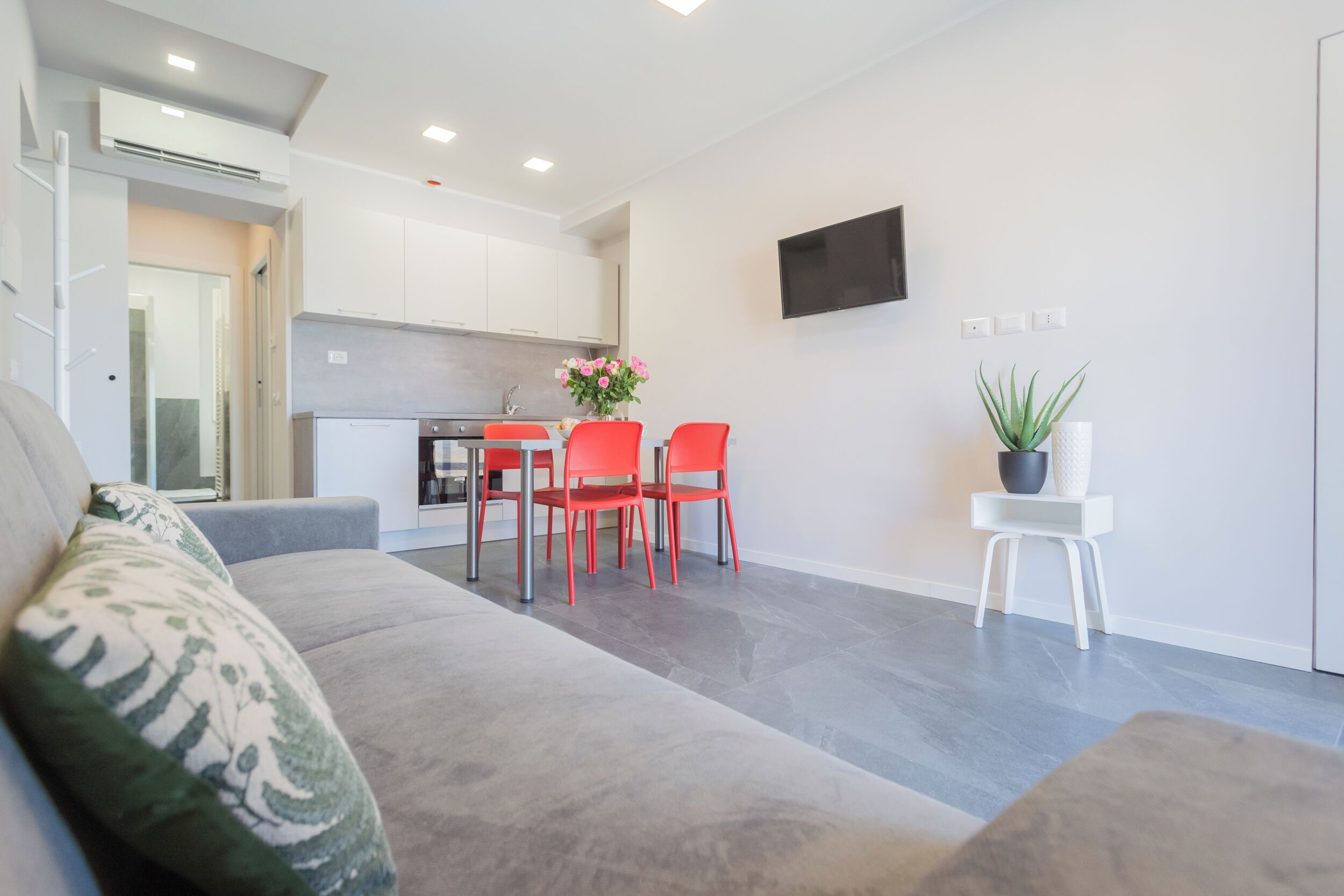A modern living room with a grey sofa, red chairs, a small table, and a potted plant.