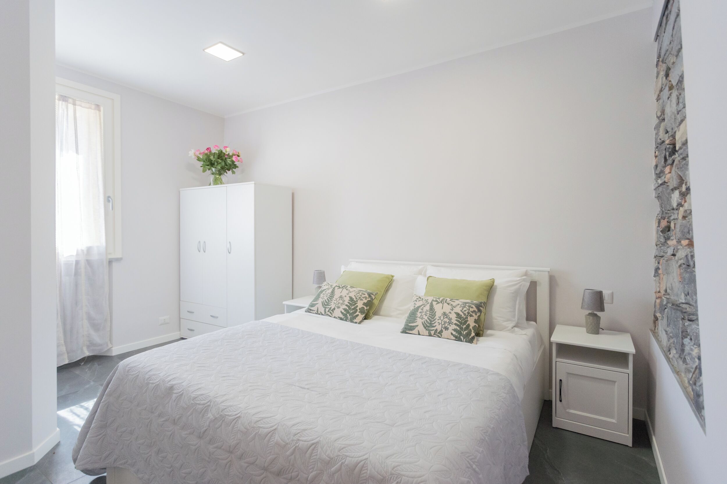 A bedroom with a large bed, white wardrobe, bedside tables, and a window with curtains.