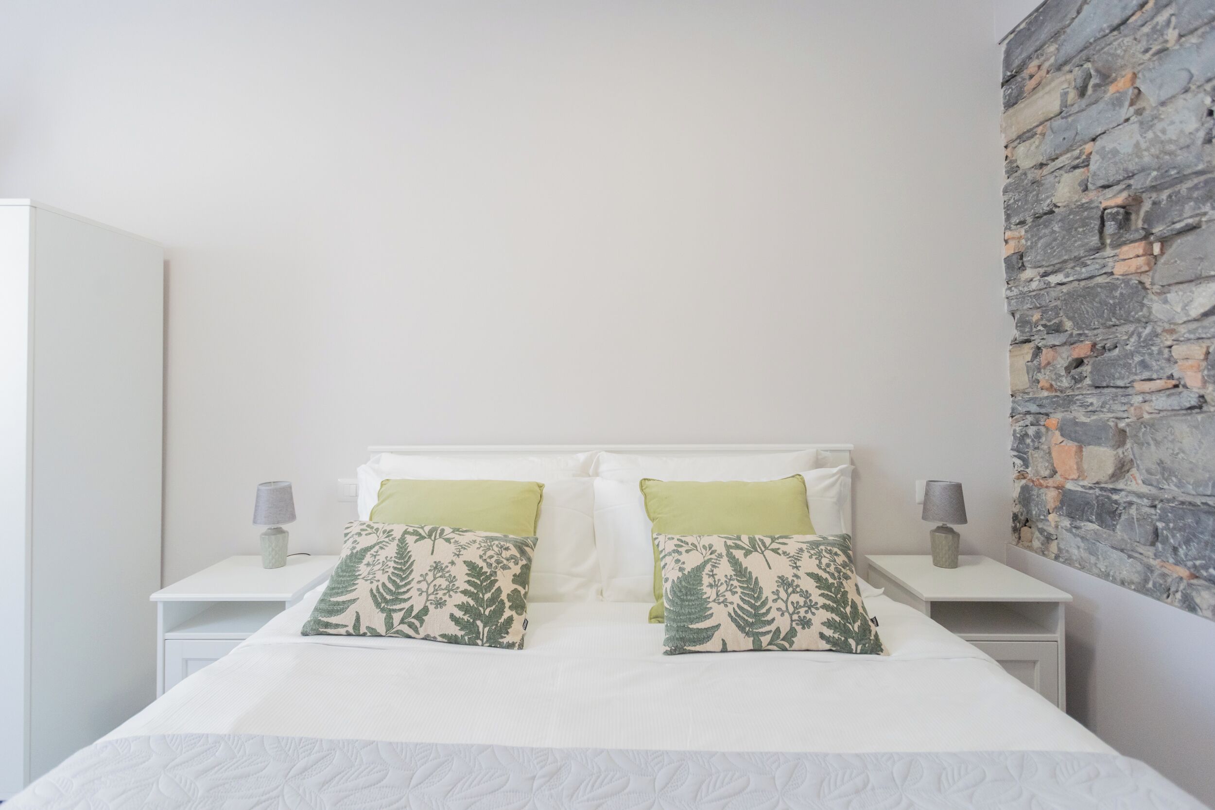 Un dormitorio con una cama blanca, dos mesitas de noche y una pared de piedra.