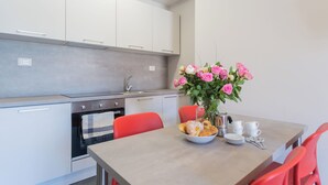 A modern kitchen with white cabinets, a stainless steel oven, and a dining table set with a bowl of pastries, a vase of flowers, and white cups. - Sant'Agostino Apartments by Rent all Como (Como)