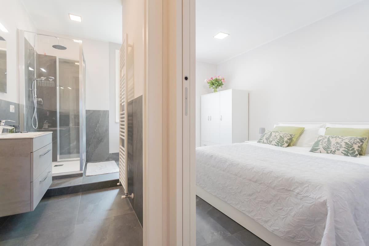 A modern hotel room with a shower, a bed with white bedding, and a white wardrobe.