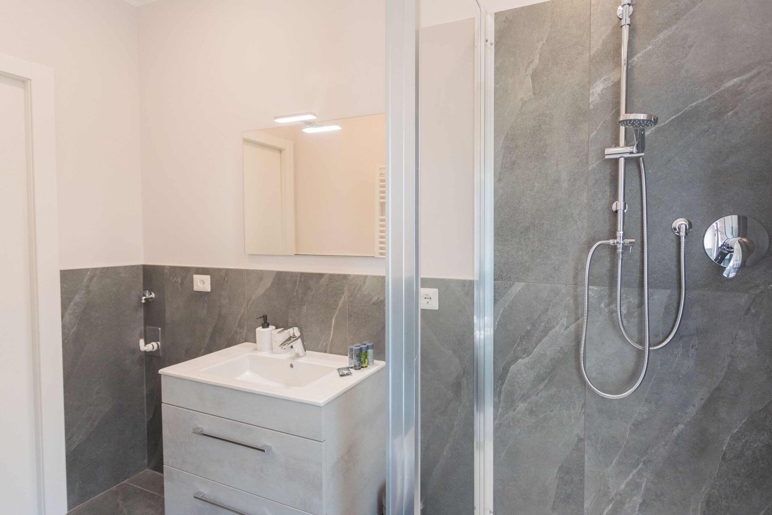 Un baño moderno con ducha de vidrio, lavamanos blanco y pared con azulejos de mármol.