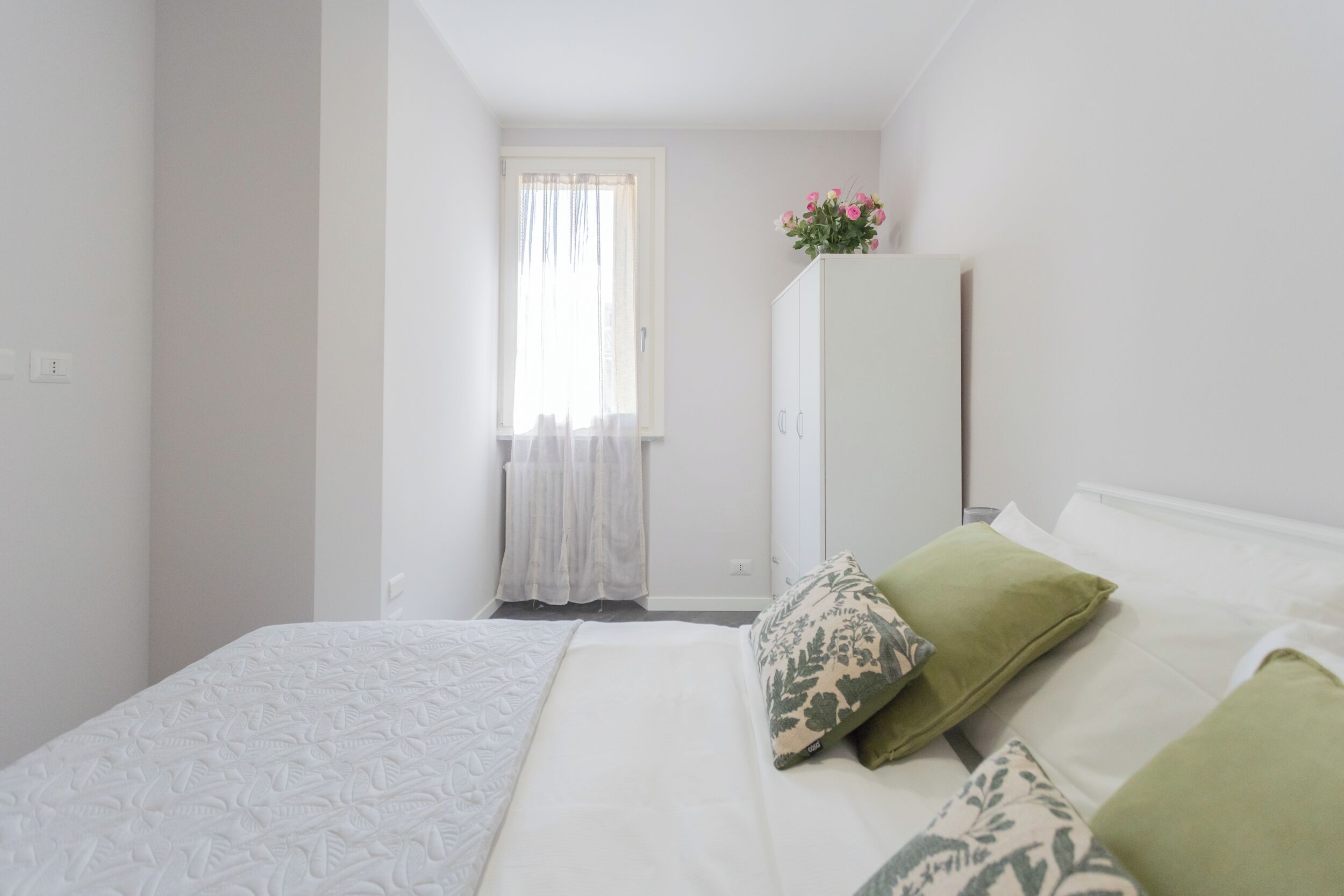 A bedroom with a bed, pillows, a wardrobe, and a window with curtains.