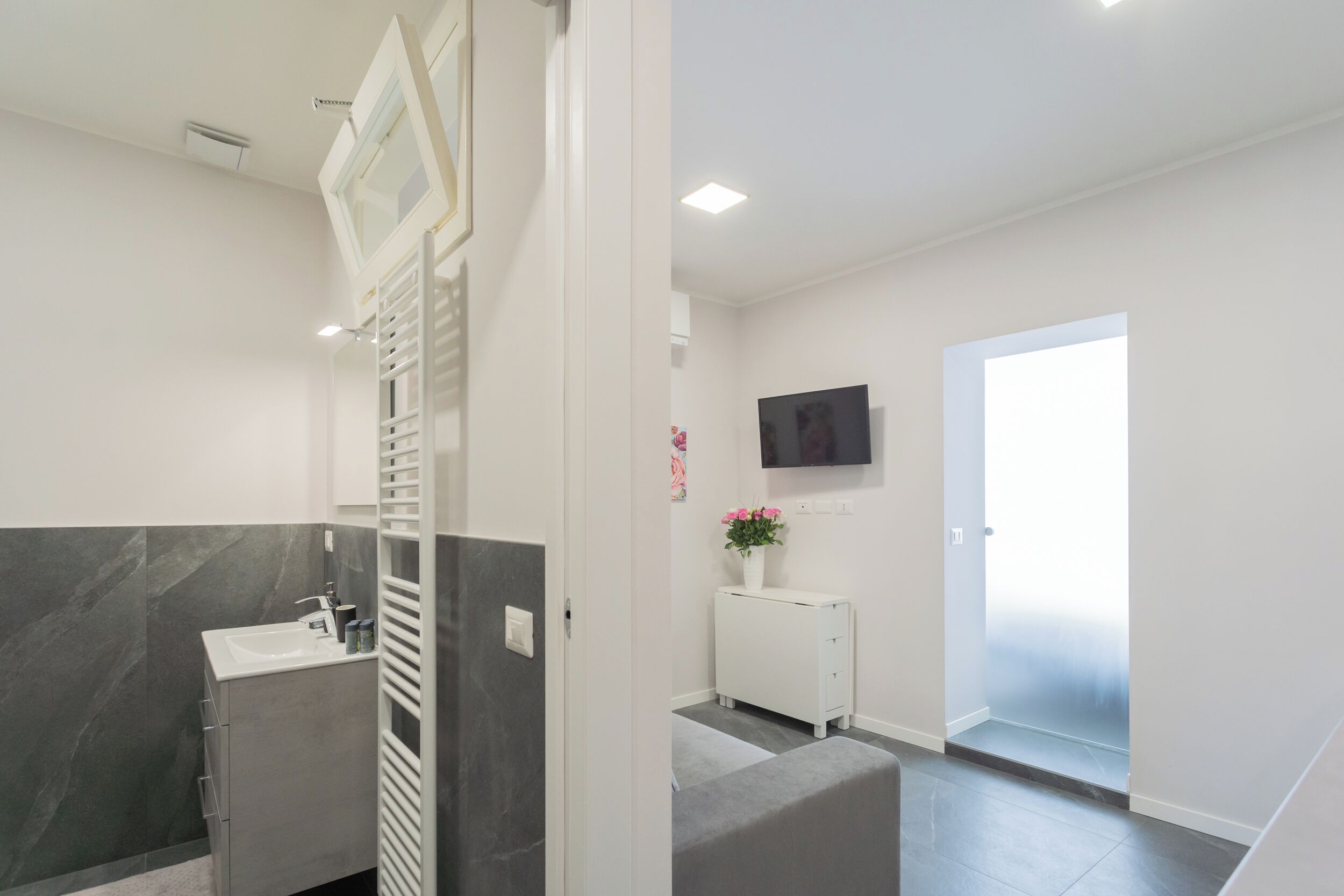 A modern bathroom with a marble wall, a white sink, and a white cabinet.