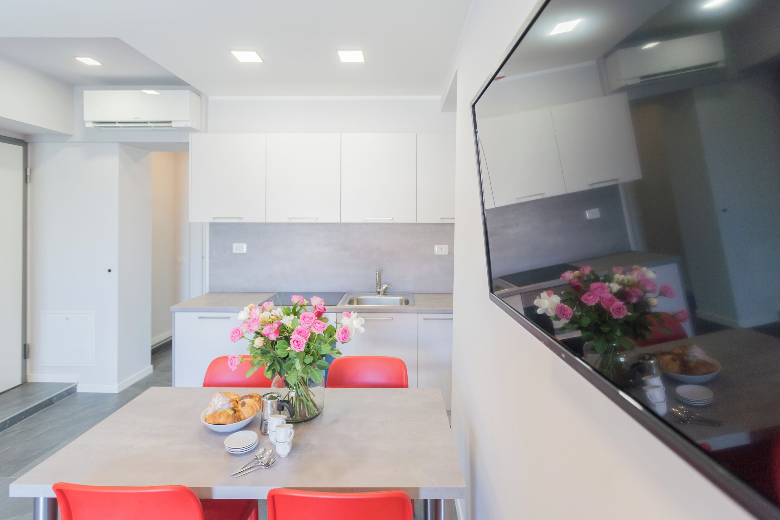 A modern kitchen with white cabinets, a dining table with red chairs, and a vase of flowers.