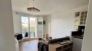A modern apartment with a dining area, a sofa, a small kitchen, and a balcony with a view of buildings. - Apartment in residence with swimming pool, near Pontaillac page and casino (Vaux-sur-Mer)