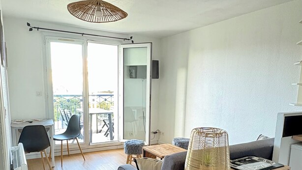 A modern living room with a sofa, a wooden coffee table, a hanging light fixture, and a sliding glass door leading to an outdoor area. - Apartment in residence with swimming pool, near Pontaillac page and casino (Vaux-sur-Mer)