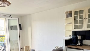 A modern living space with a sofa, a wooden coffee table, a small stool, and a kitchen area with cabinets and a refrigerator. - Apartment in residence with swimming pool, near Pontaillac page and casino (Vaux-sur-Mer)