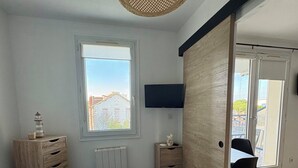 A bedroom with a bed, a dresser, a TV, a window, and a door leading to a balcony. - Apartment in residence with swimming pool, near Pontaillac page and casino (Vaux-sur-Mer)