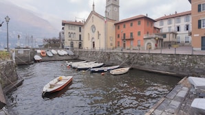 Un canal con barcos amarrados, una iglesia con un campanario y edificios a lo largo de la orilla.